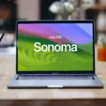 MacBook Pro sobre una mesa de madera con el fondo de pantalla de macOS Sonoma y su nombre en el centro